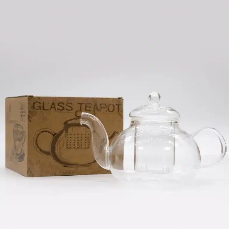 A clear glass teapot with a lid is placed next to a brown cardboard box labeled