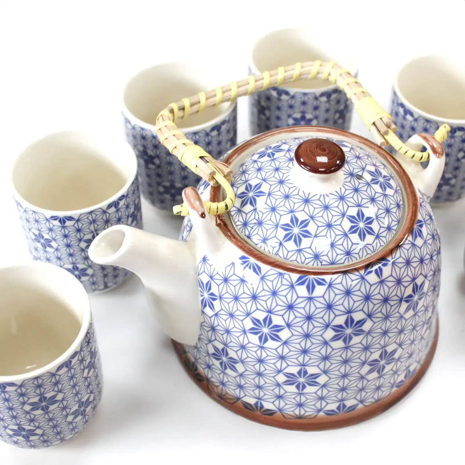 A ceramic teapot with a woven handle and blue geometric pattern is surrounded by six matching cups, all on a white background.