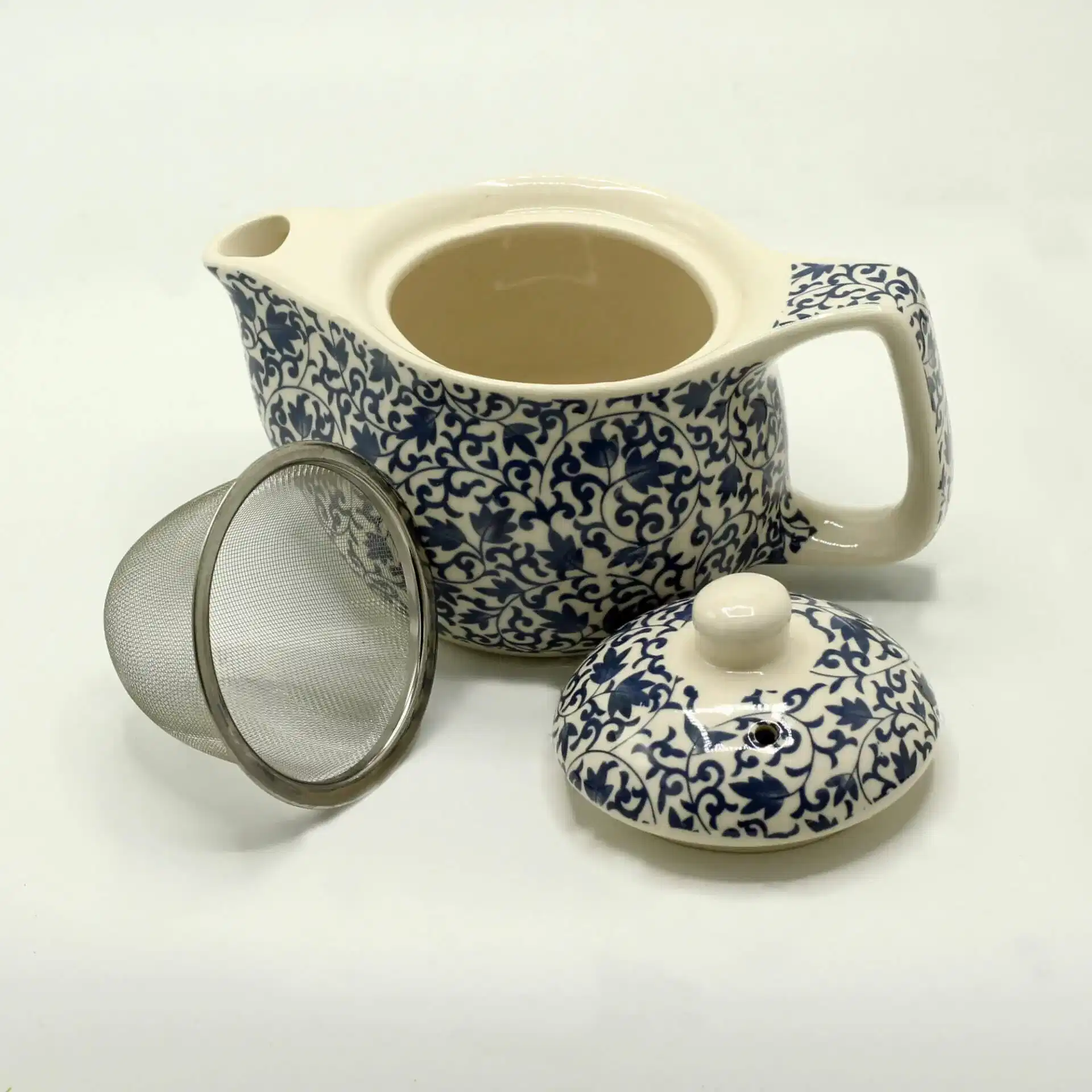 A ceramic teapot with a blue and white floral pattern, shown with its matching lid removed and a metal mesh tea infuser beside it.