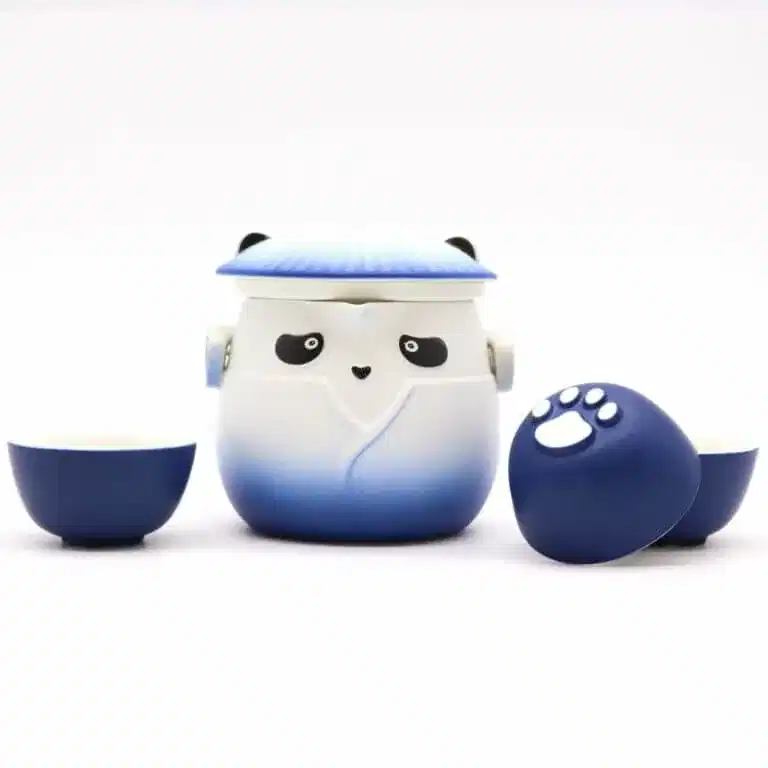 A blue and white panda-shaped teapot with a lid, flanked by two matching teacups, one turned to show a white paw print on its base.