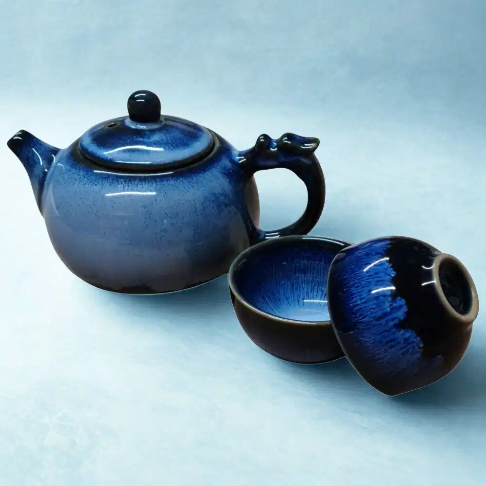 The Ocean Blue Teapot for One | Aqua Teal Tea Set with 2 Cups, featuring a dragon-shaped handle, is displayed beside the matching cups against a light blue background.
