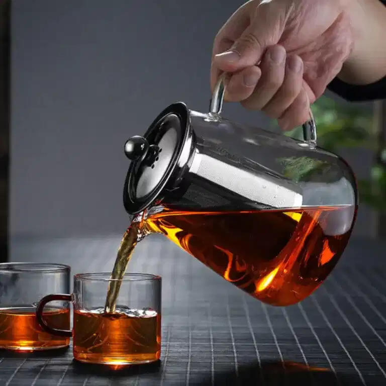 Pouring tea from a Premium Borosilicate Glass Teapot with Tea Infuser | Extra-Thick Design into two clear glass mugs on a table.