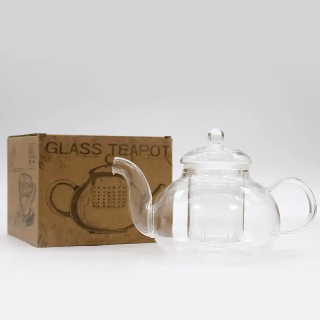 A clear glass teapot with a lid is placed next to a brown cardboard box labeled 