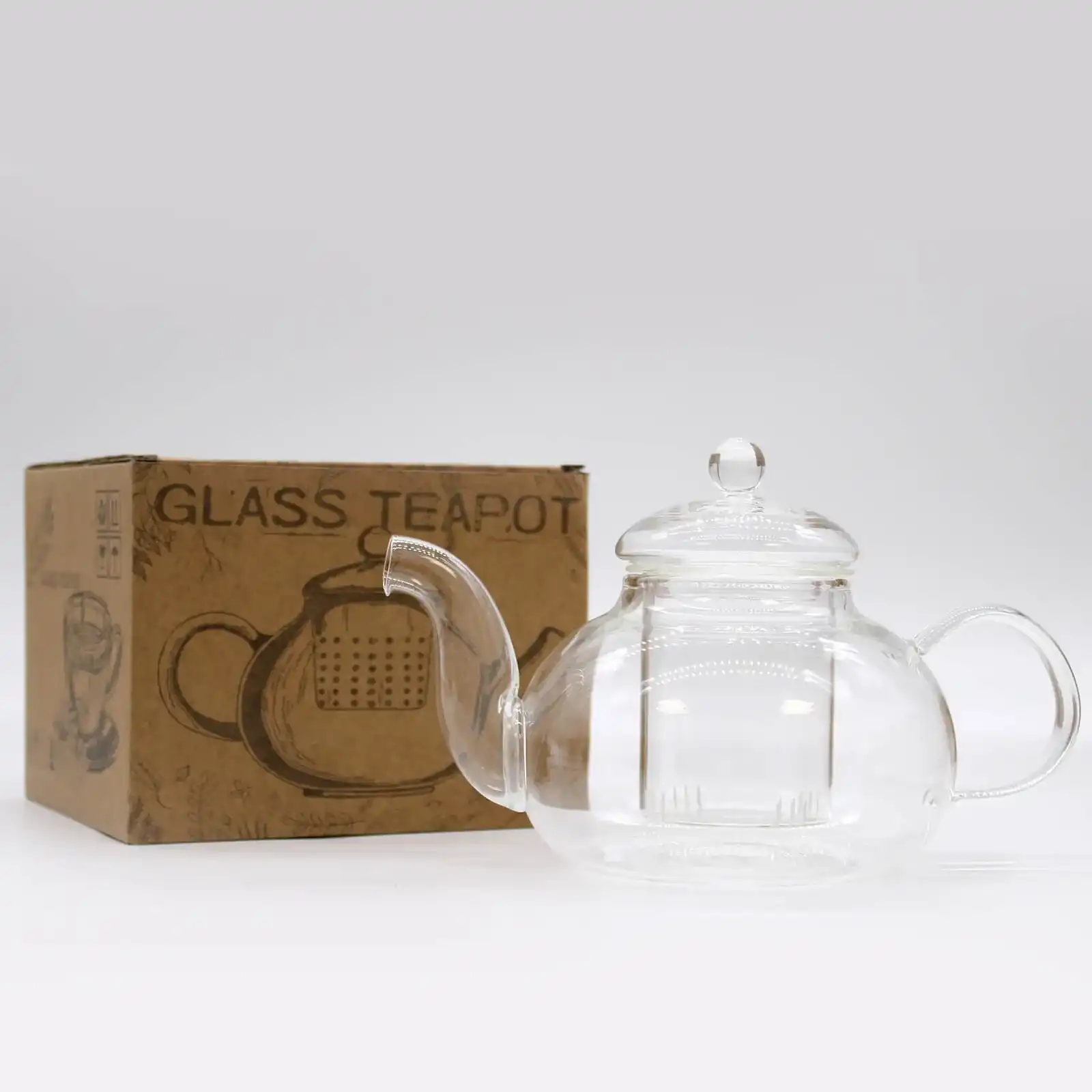 A clear glass teapot with a lid is placed next to a brown cardboard box labeled 