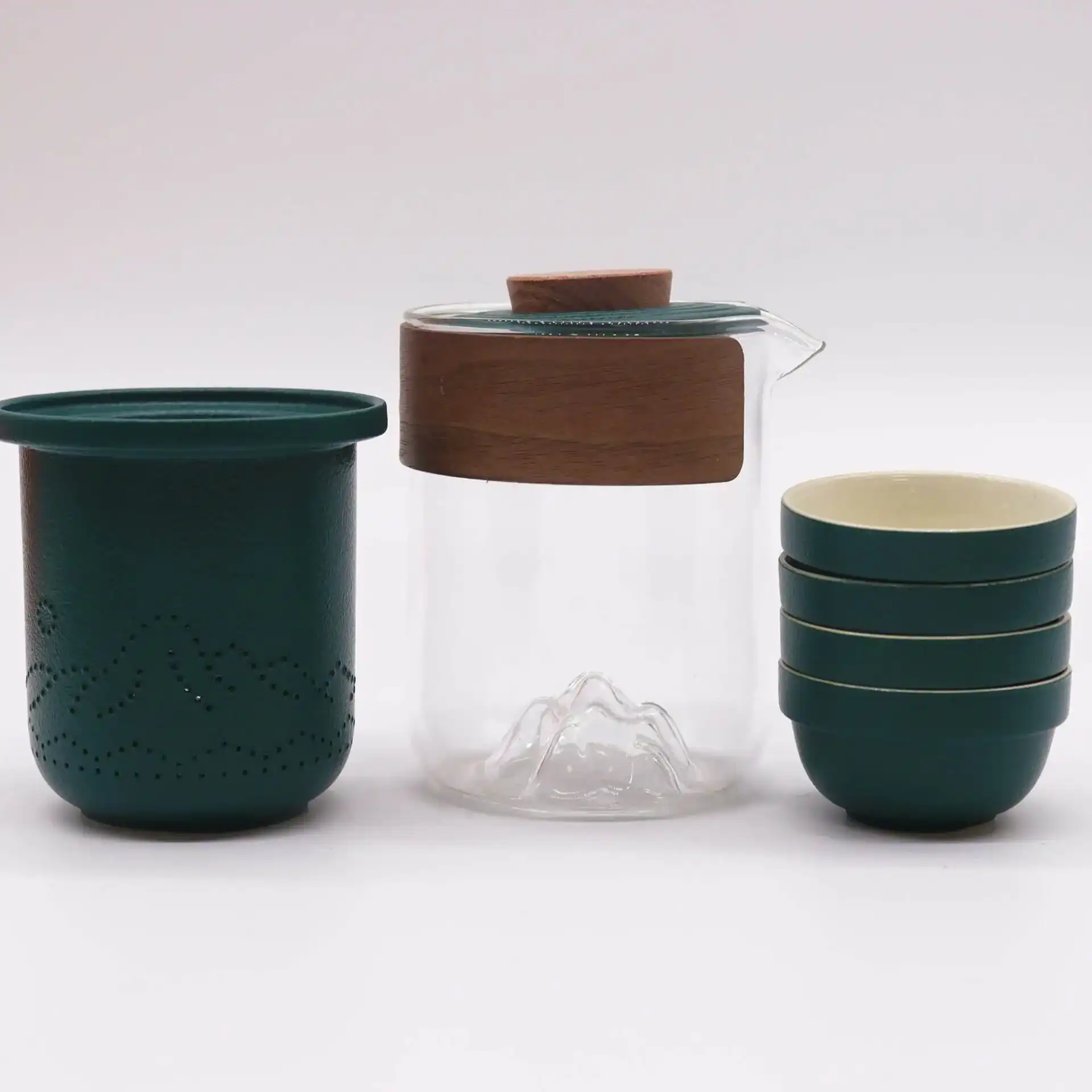 A teal textured container, a clear glass pitcher with a wooden band and mountain-shaped base, and a stack of four teal cups are displayed against a plain white background.