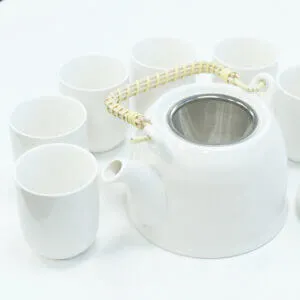 A white teapot with a woven handle and metal strainer is surrounded by six matching white cups on a white surface.