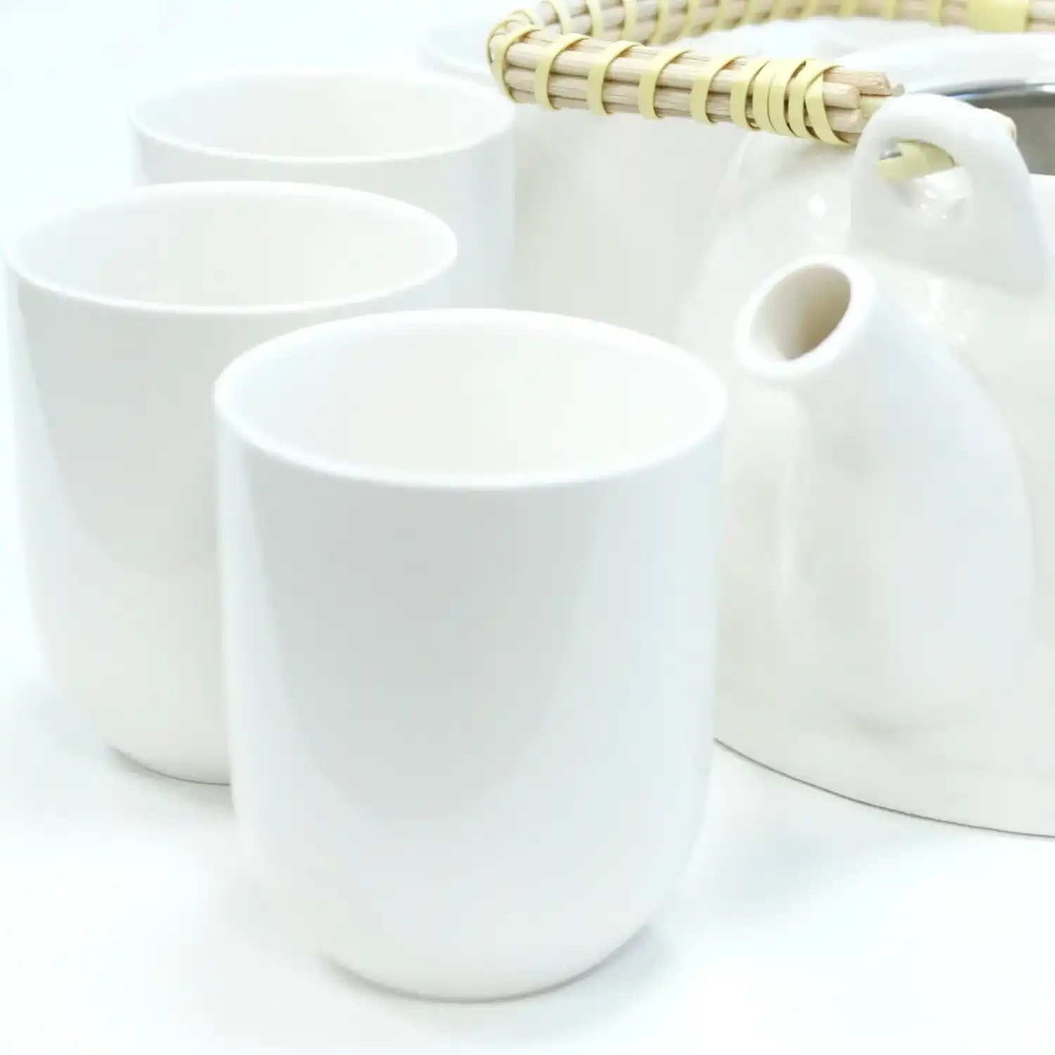 Three white ceramic cups and a white teapot with a woven handle are placed on a white surface.