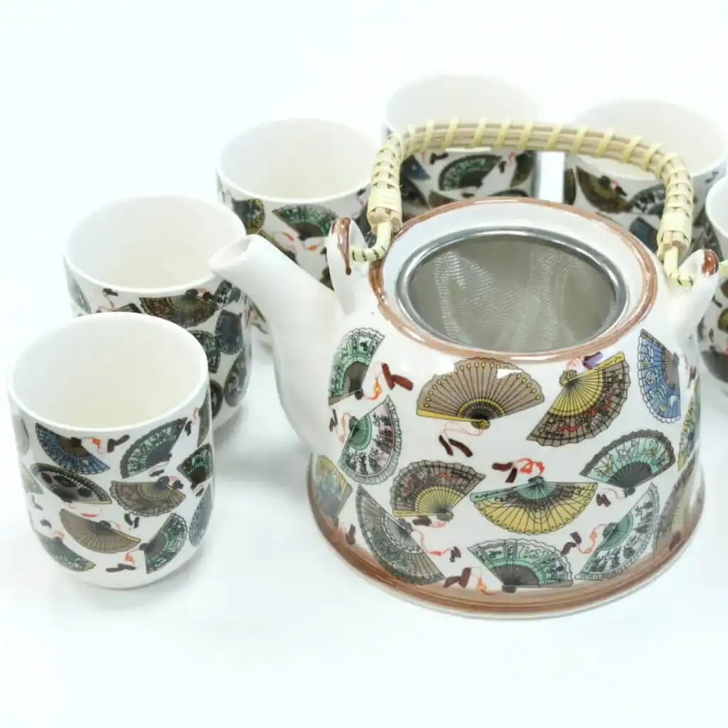 A ceramic teapot with a woven handle and matching cups, all decorated with colorful fan patterns, are arranged on a white surface.