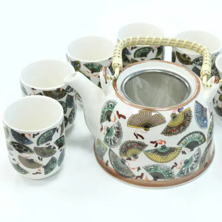 A ceramic teapot with a woven handle and matching cups, all decorated with colorful fan patterns, are arranged on a white surface.