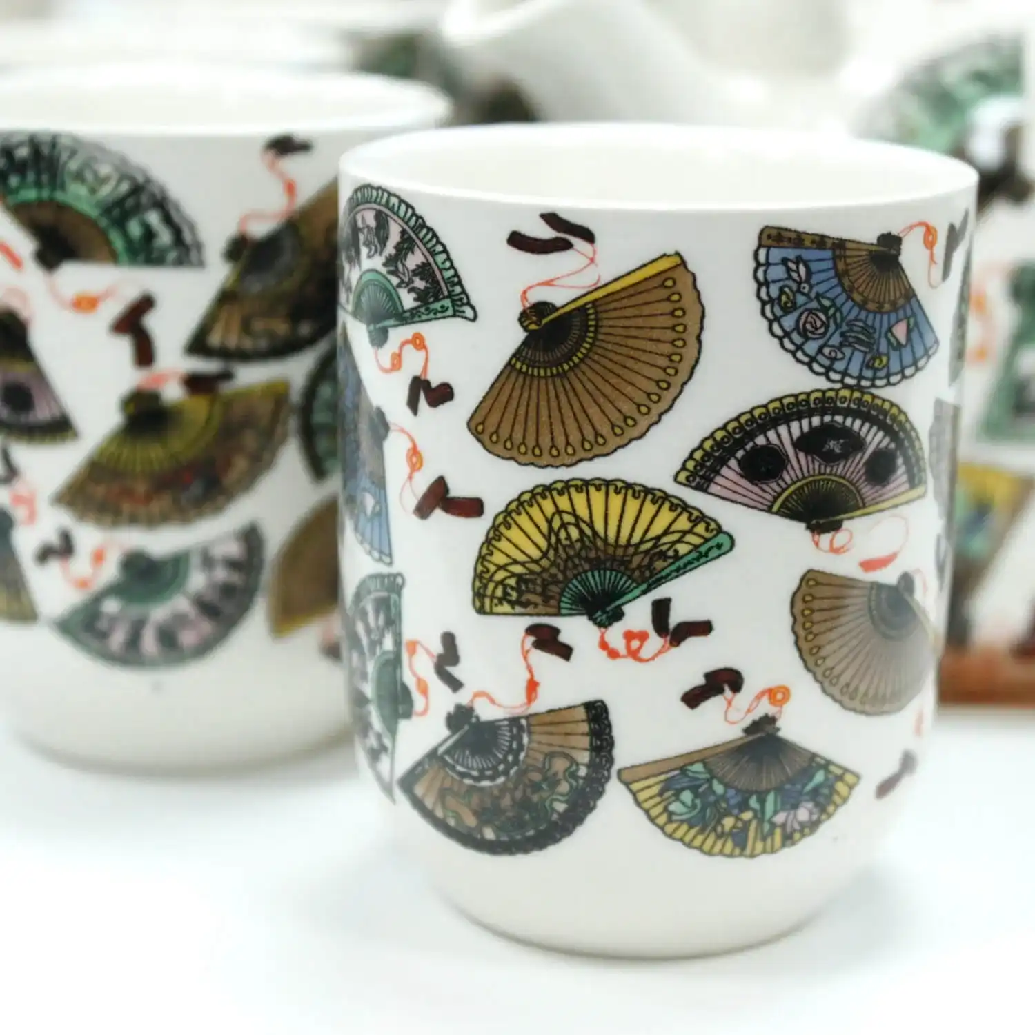 White ceramic cups decorated with colorful, detailed illustrations of folding fans and red ribbons.