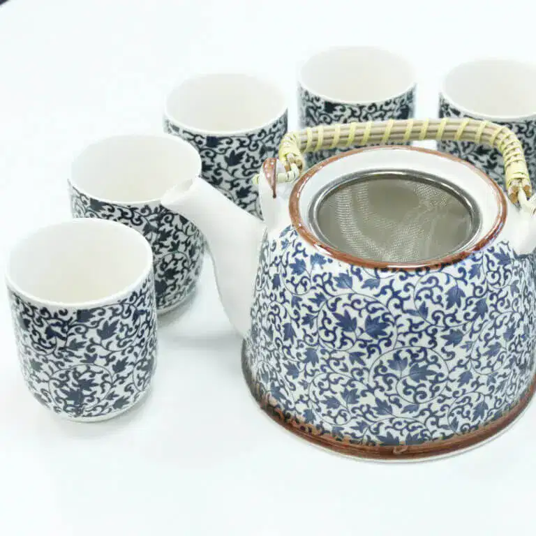 A ceramic teapot with a woven handle and six matching teacups, all featuring a blue and white floral pattern, arranged on a white surface.