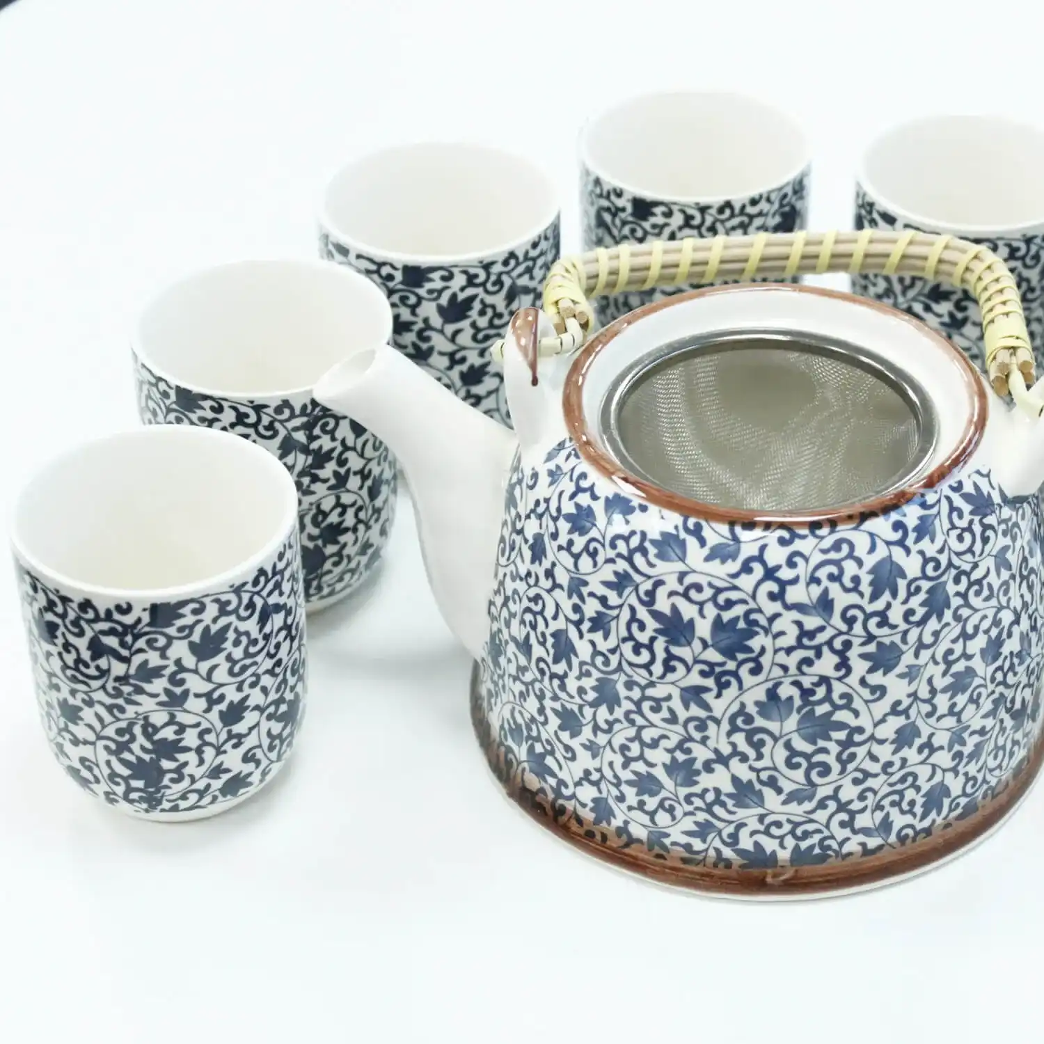 A ceramic teapot with a woven handle and six matching teacups, all featuring a blue and white floral pattern, arranged on a white surface.