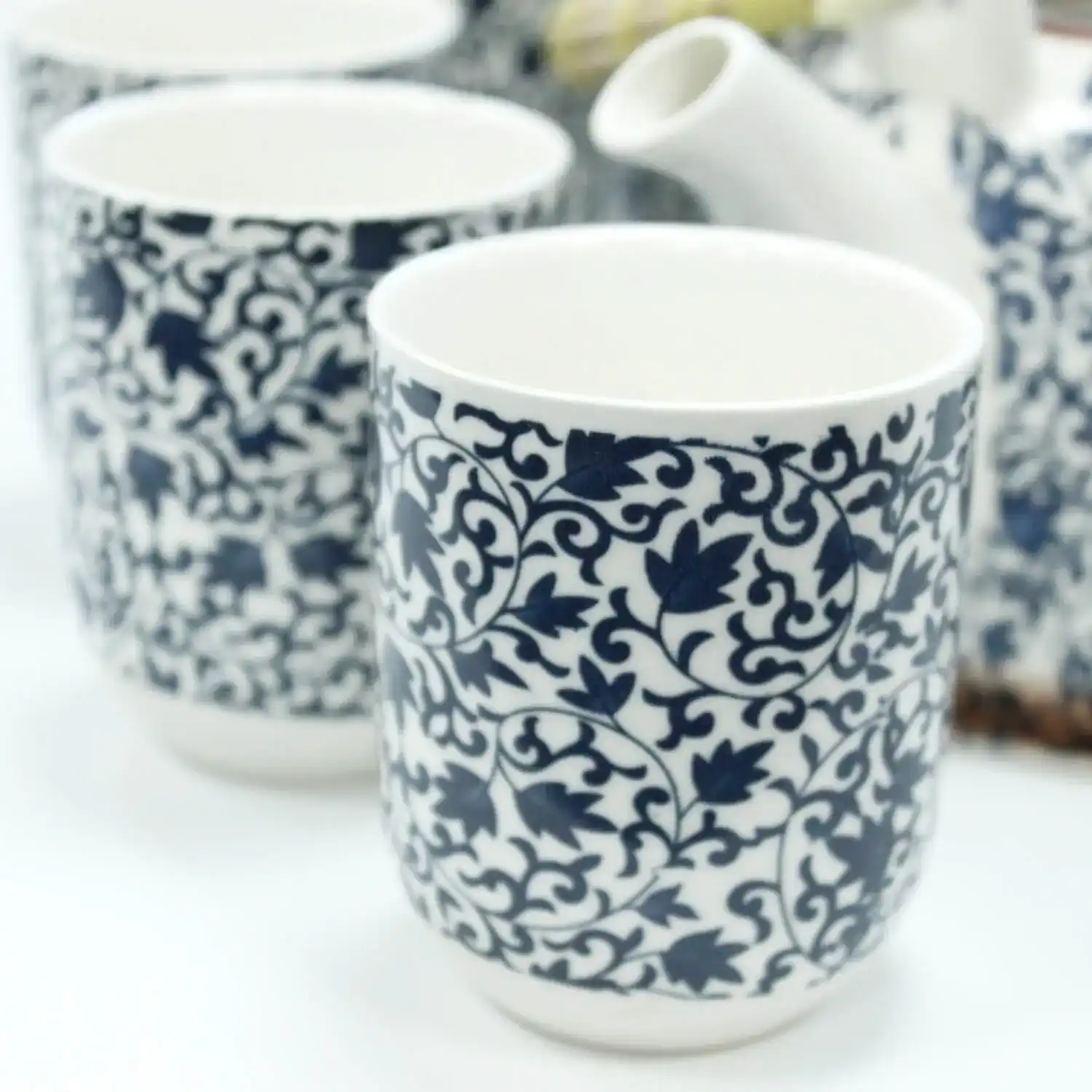 Close-up of white ceramic cups with intricate dark blue floral patterns, accompanied by a matching teapot in the background.