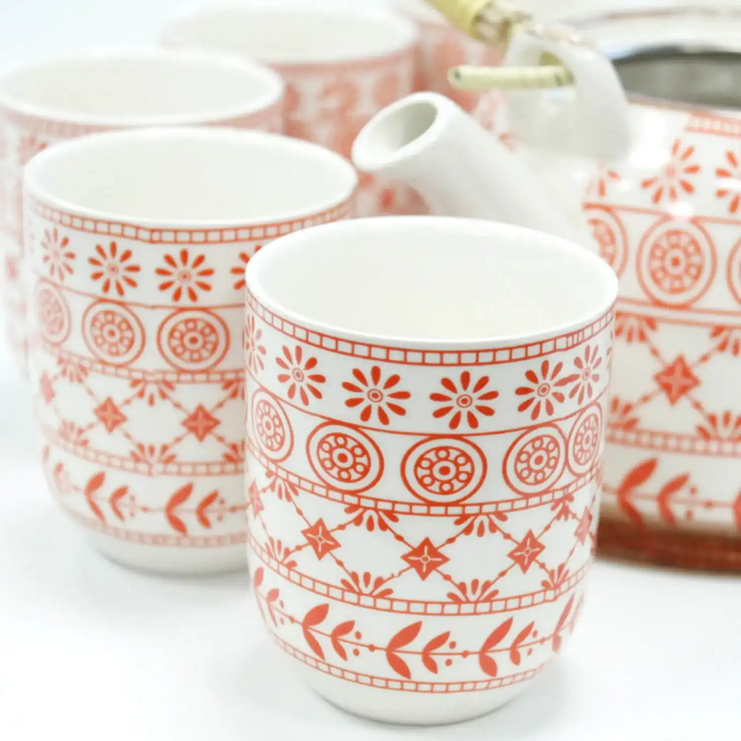 White ceramic tea set with cups and a teapot, all featuring red geometric and floral patterns.