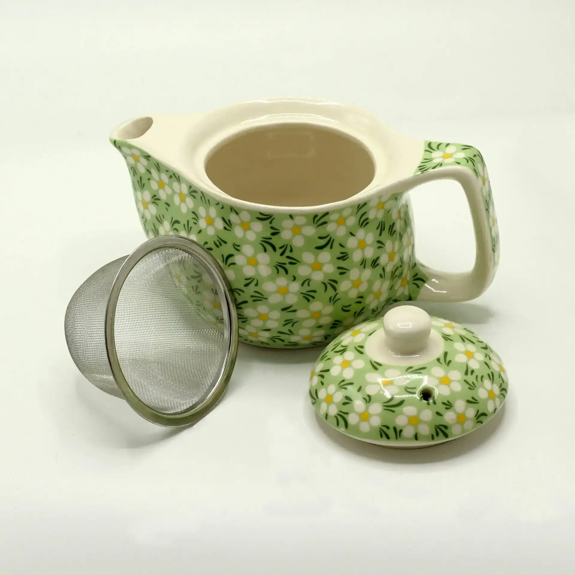 A ceramic teapot with a green and white floral pattern, shown with its lid and a metal tea infuser placed beside it.