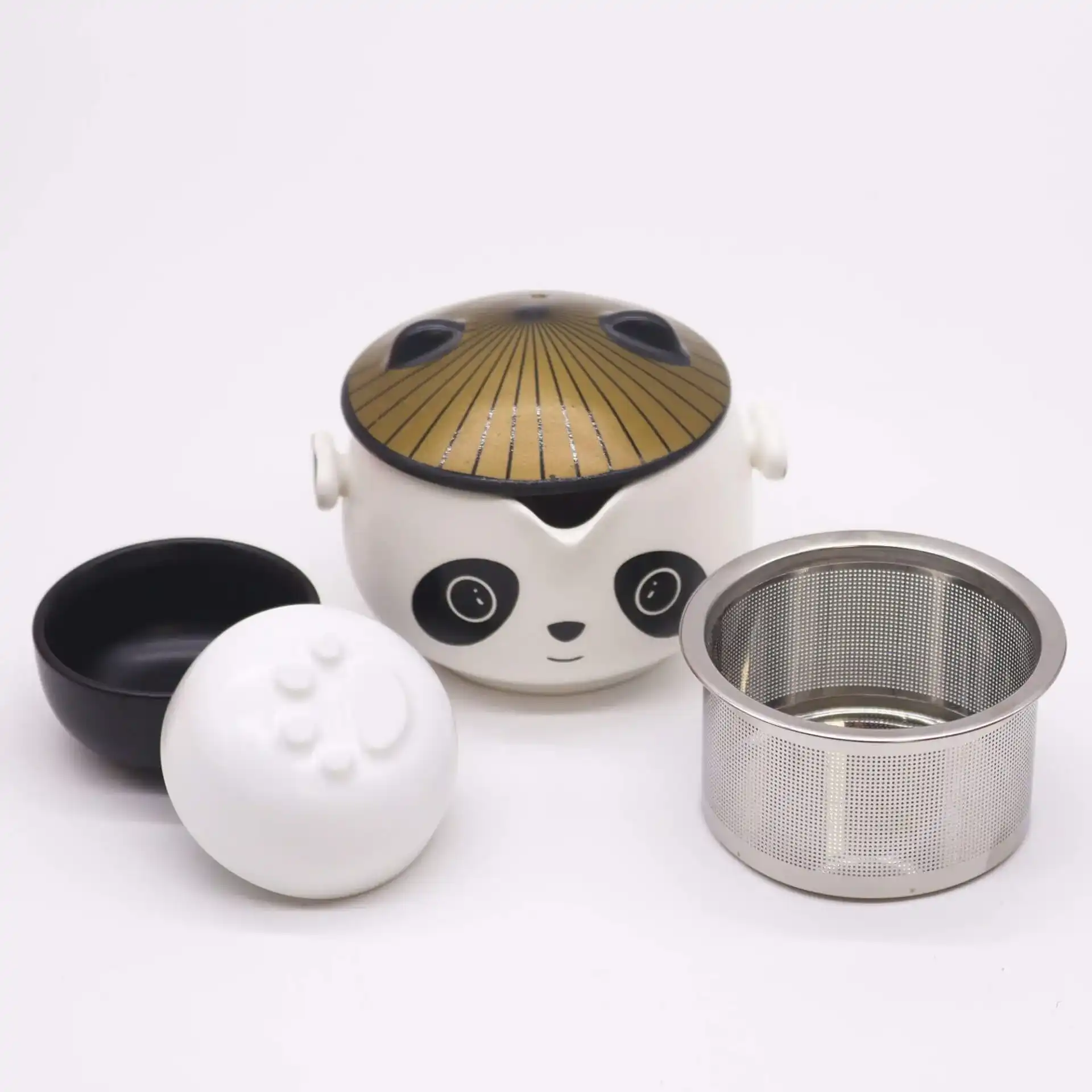 A panda-shaped teapot with a gold lid, a black bowl, a white lid, and a metal tea infuser are displayed on a white background.