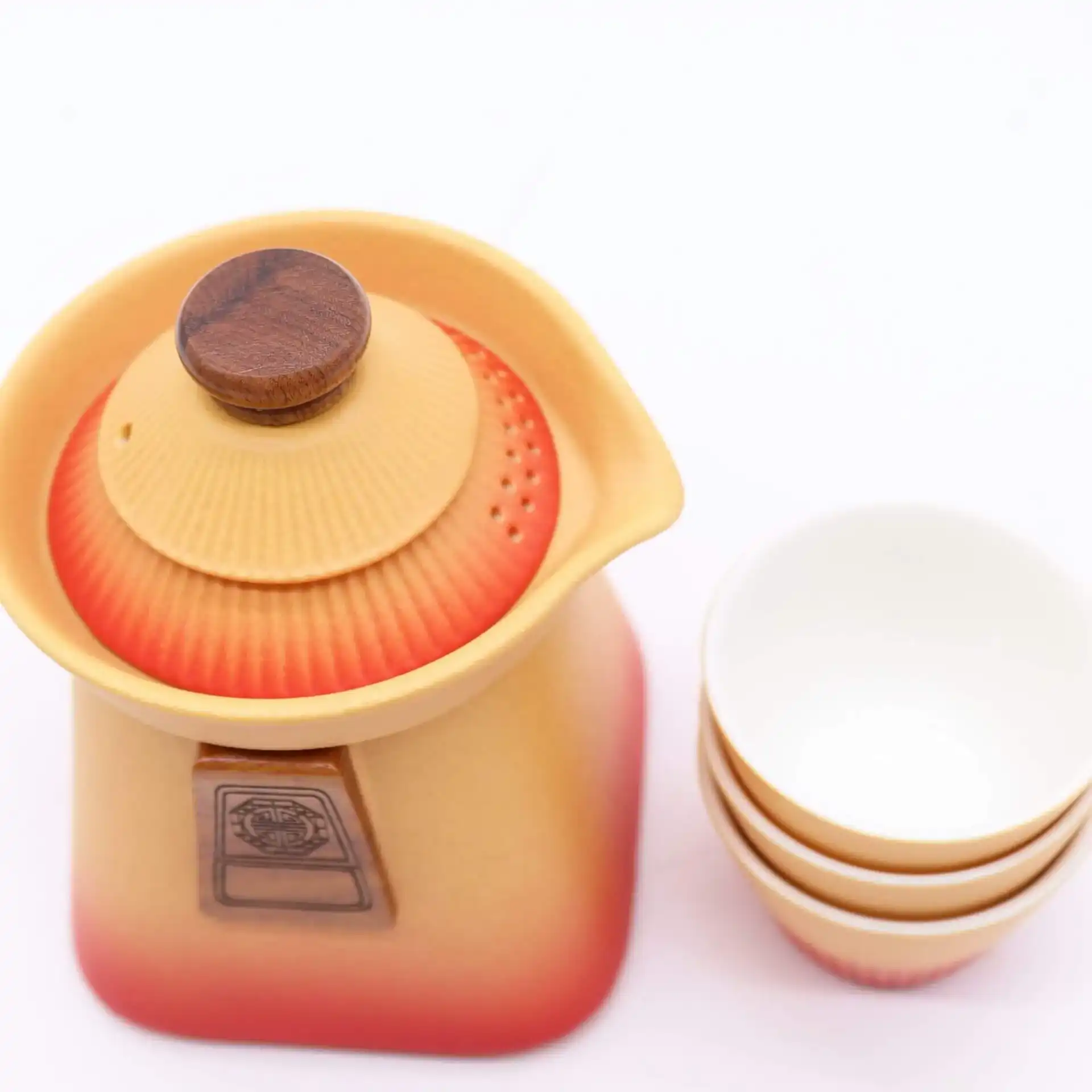 A ceramic teapot with a wooden knob on the lid is placed beside a stack of three empty white teacups against a white background.
