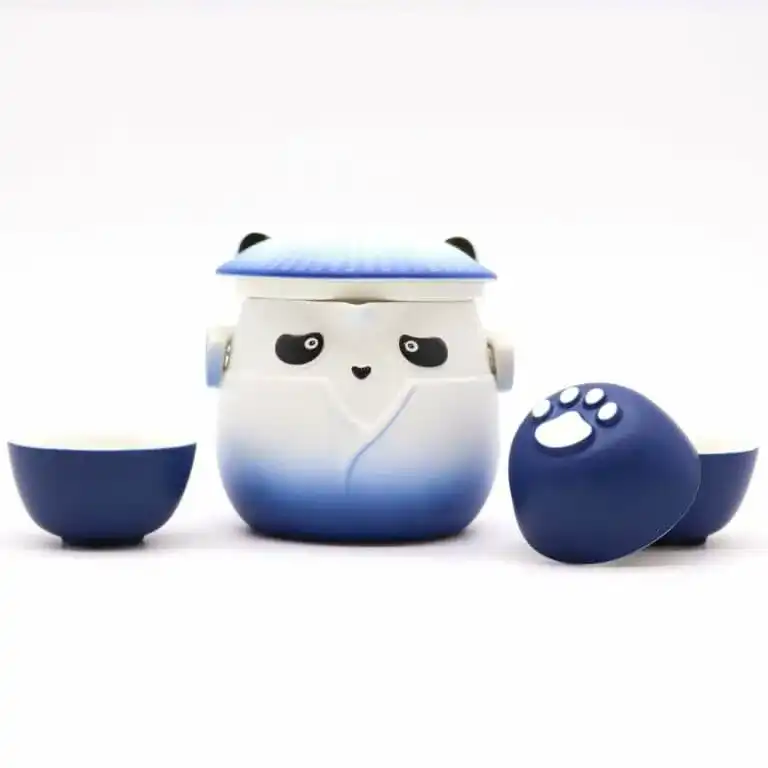 A blue and white panda-shaped teapot with a lid, flanked by two matching teacups, one turned to show a white paw print on its base.