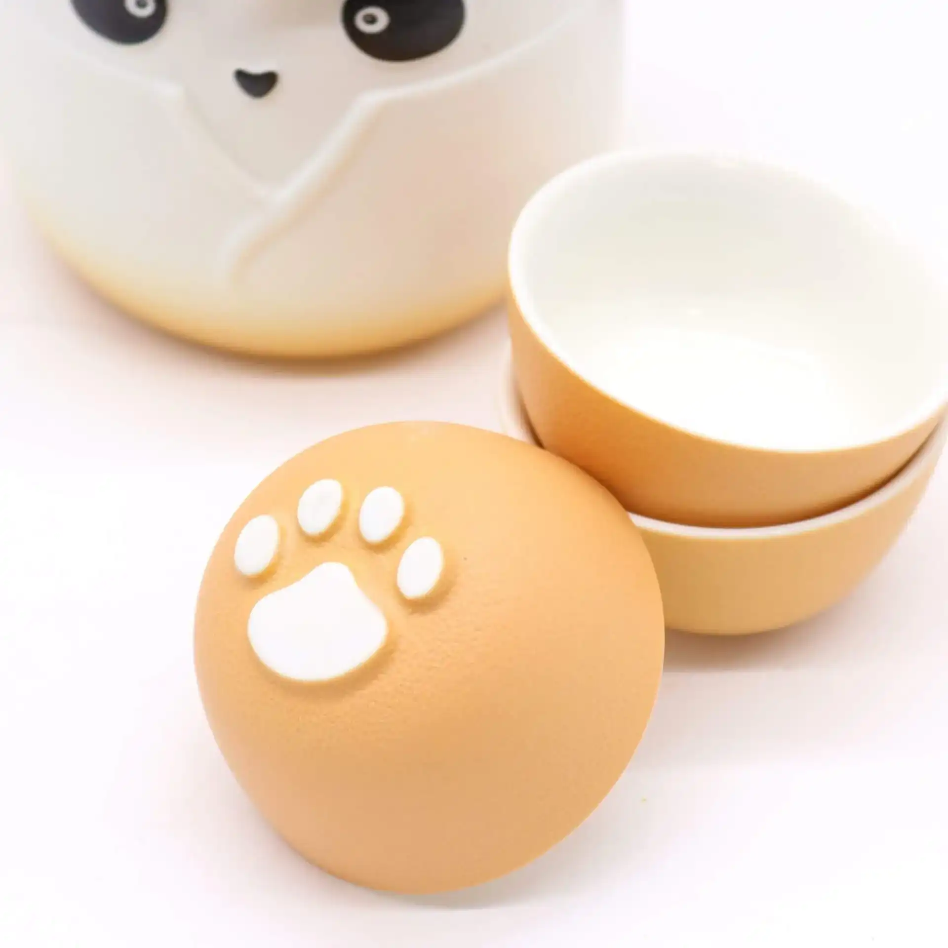 Two small ceramic bowls are stacked next to another bowl showing its base, which features a white paw print design. Part of a larger container with a panda face is also visible.