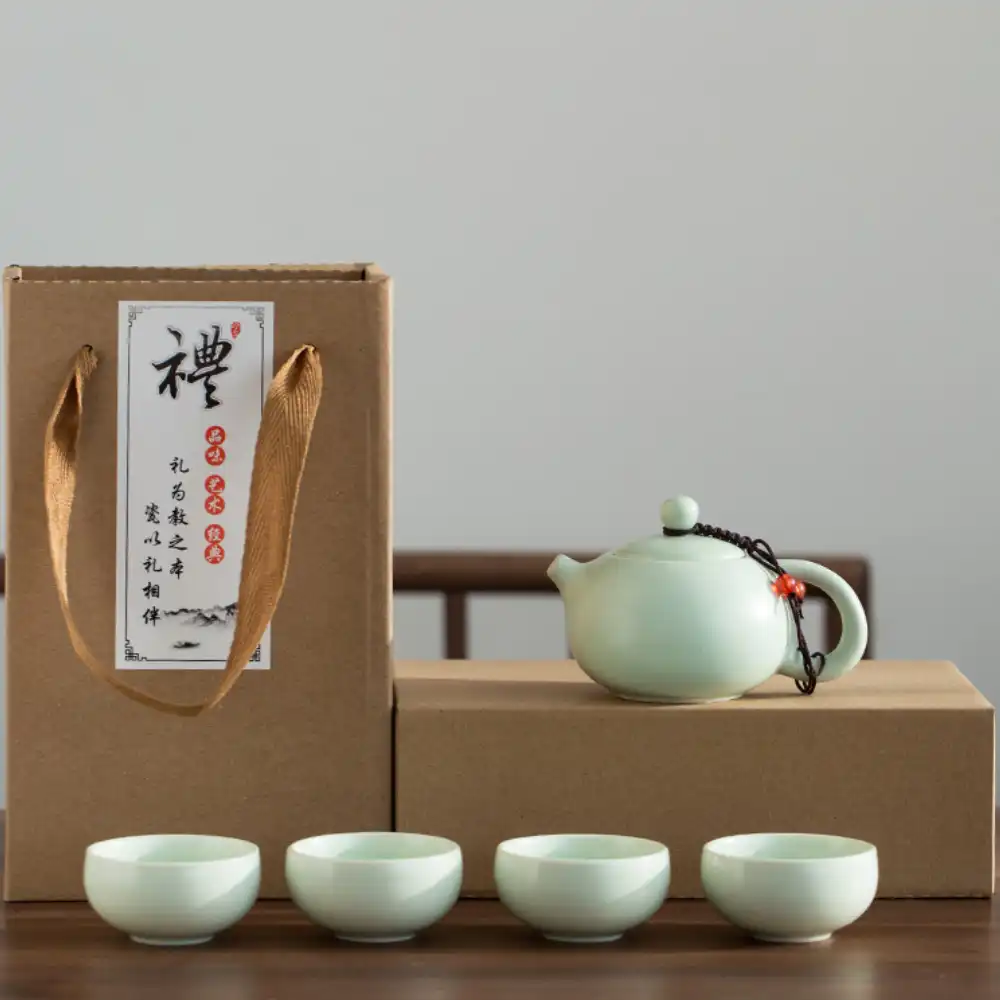 A ceramic teapot with four matching cups is displayed in front of two cardboard boxes, one with a rope handle and a label featuring Chinese calligraphy.