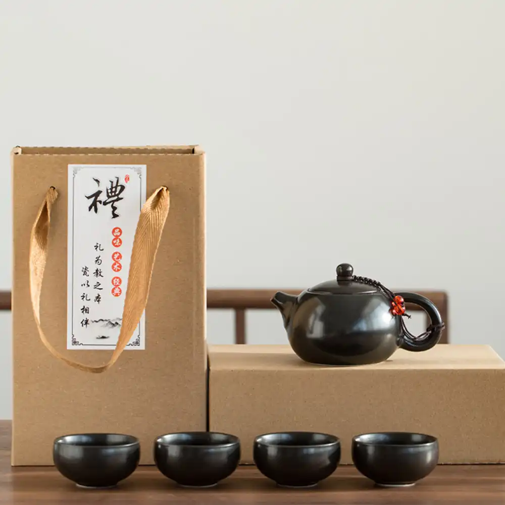 A black ceramic teapot with four matching teacups is displayed beside two brown gift boxes, one with rope handles and Chinese characters on a white label.