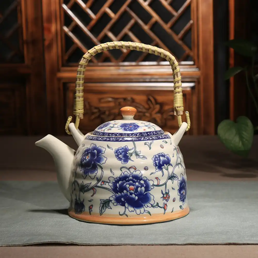 A ceramic teapot with a floral blue and white design and a woven bamboo handle sits on a cloth-covered table.