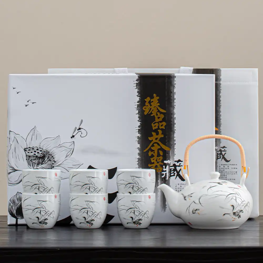 A white porcelain tea set with a teapot and six cups featuring black floral designs, displayed in front of decorative packaging with Chinese characters.