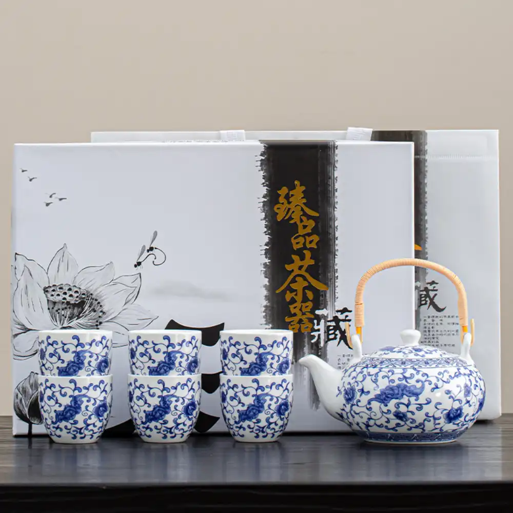 A blue and white porcelain tea set with a teapot and four cups is displayed in front of decorative packaging with floral and calligraphy designs.
