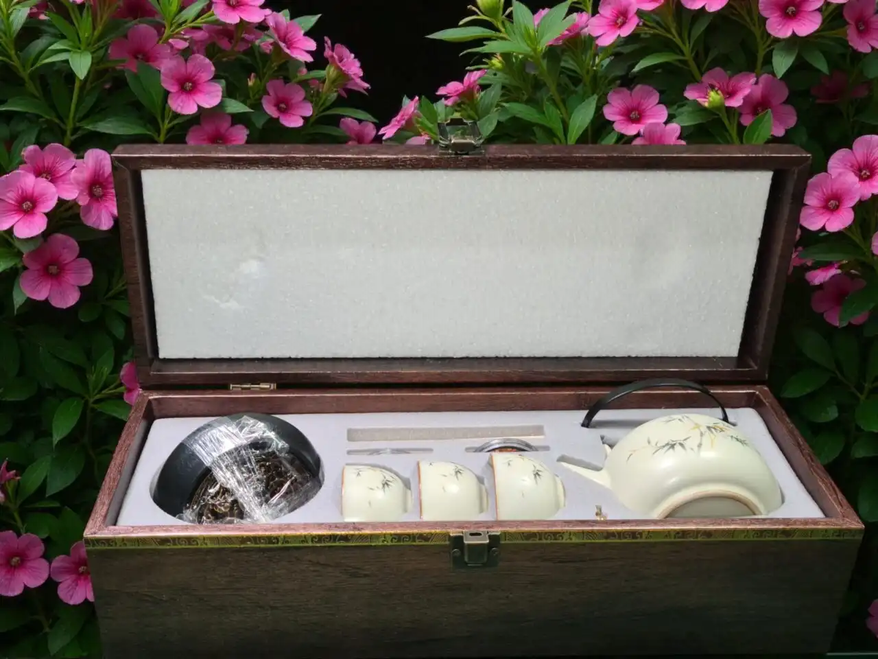 The Elegant Cream Porcelain Tea Set with Bamboo Design - 4-Piece Collection features a teapot, two cups, and accessories in a cushioned wooden box, accented by subtle bamboo details and pink flowers.