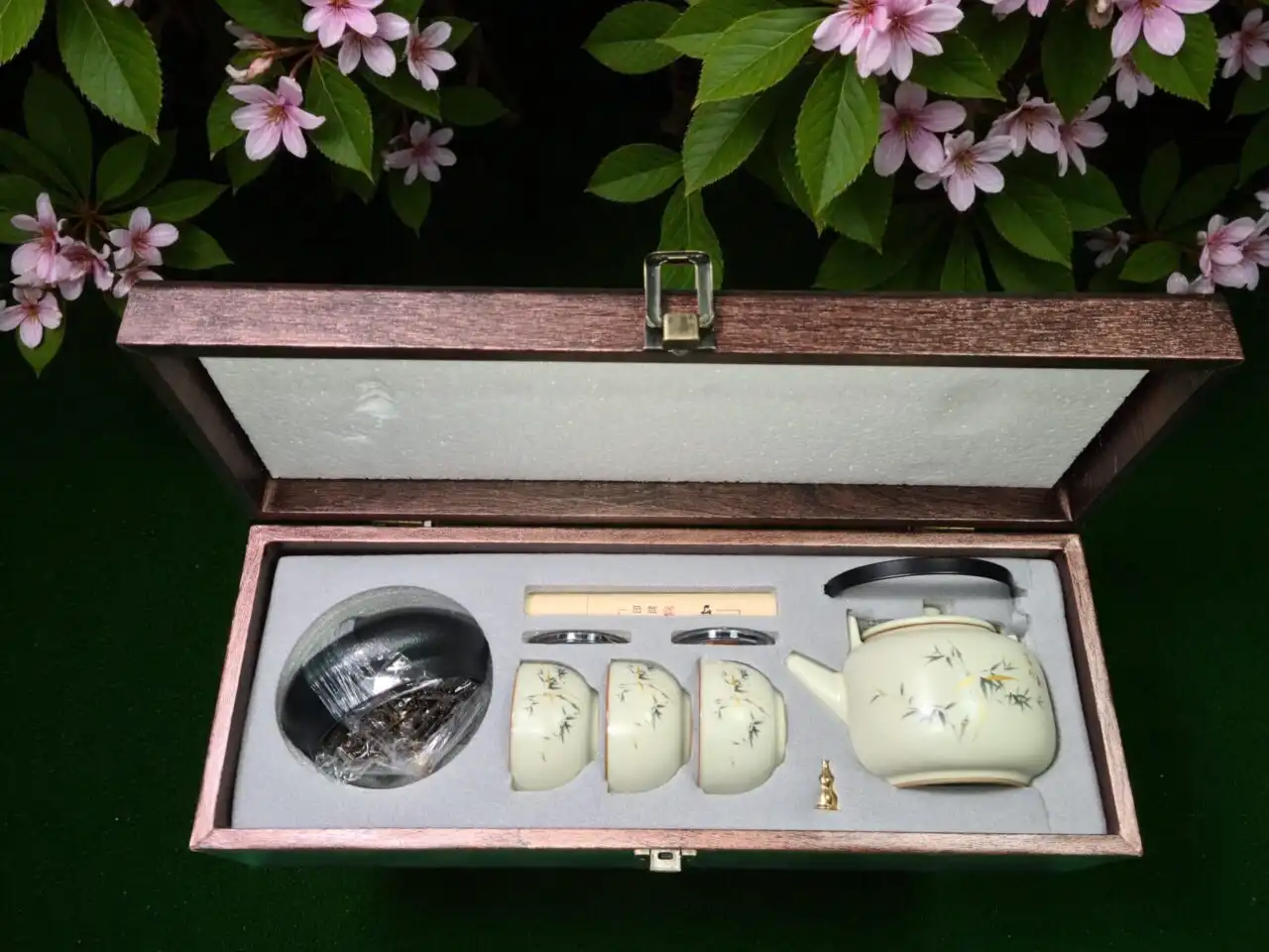 The Elegant Cream Porcelain Tea Set with Bamboo Design - 4-Piece Collection comes in a wooden box with foam insert and features a porcelain teapot, three cups, and subtle bamboo accents, all displayed against a floral background.