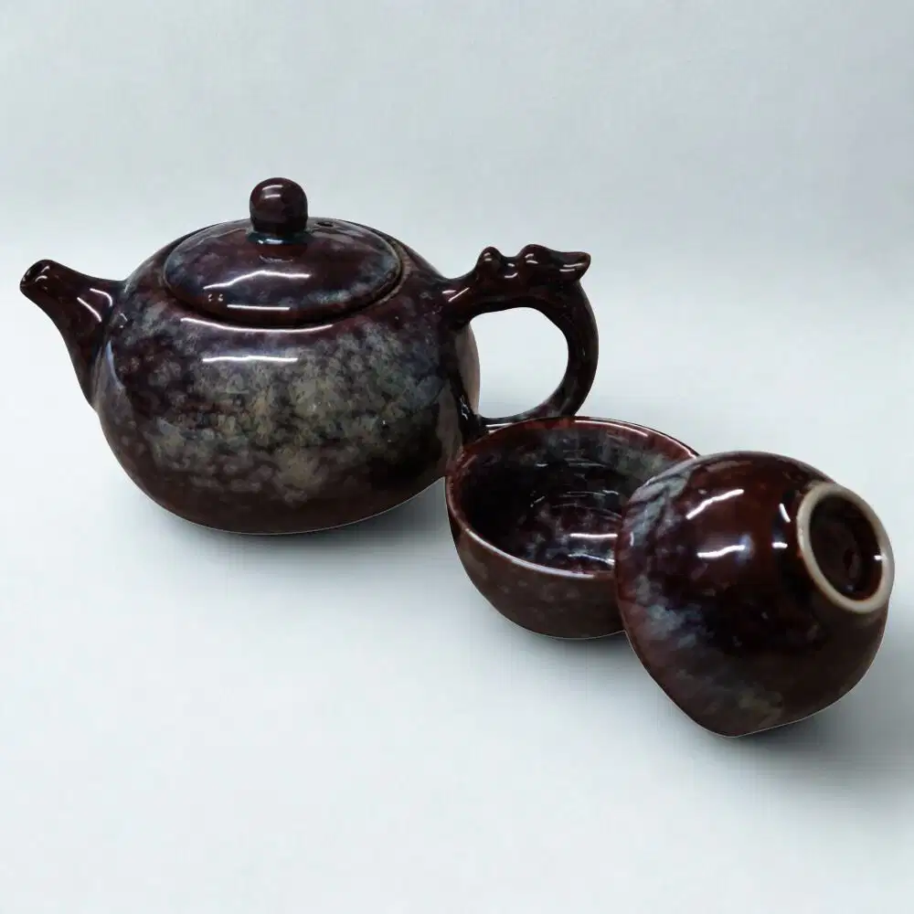 The Ocean Blue Teapot for One is an aqua teal tea set with 2 cups, featuring a glossy marbled finish and round lid, inspired by ocean hues, and elegantly displayed on a plain white background.