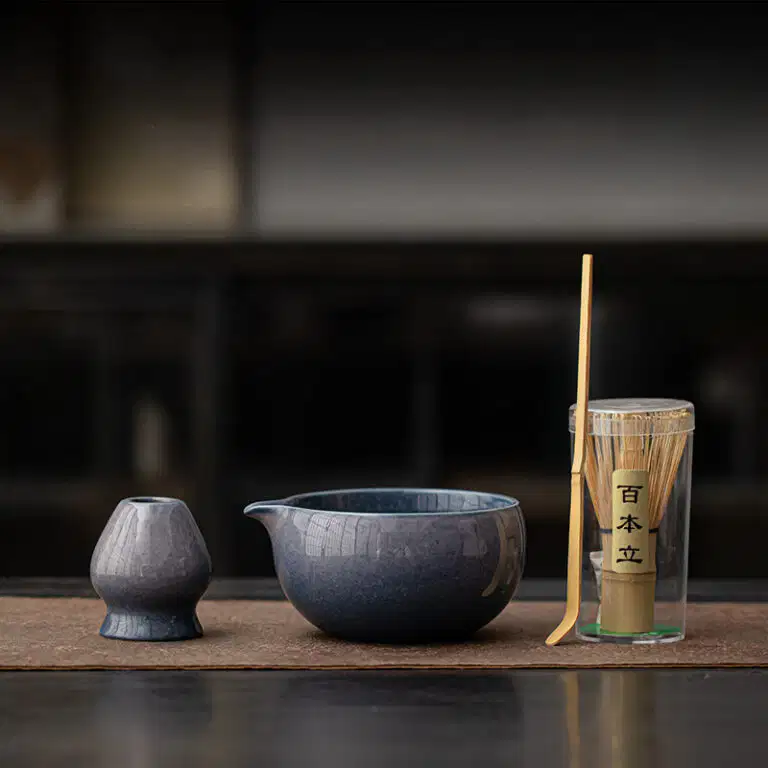 The Kiln-Glazed Matcha Set – 4 Piece | Stone includes a ceramic small pitcher, bowl, bamboo whisk, and scoop on a mat, adding elegance to your tea ritual.