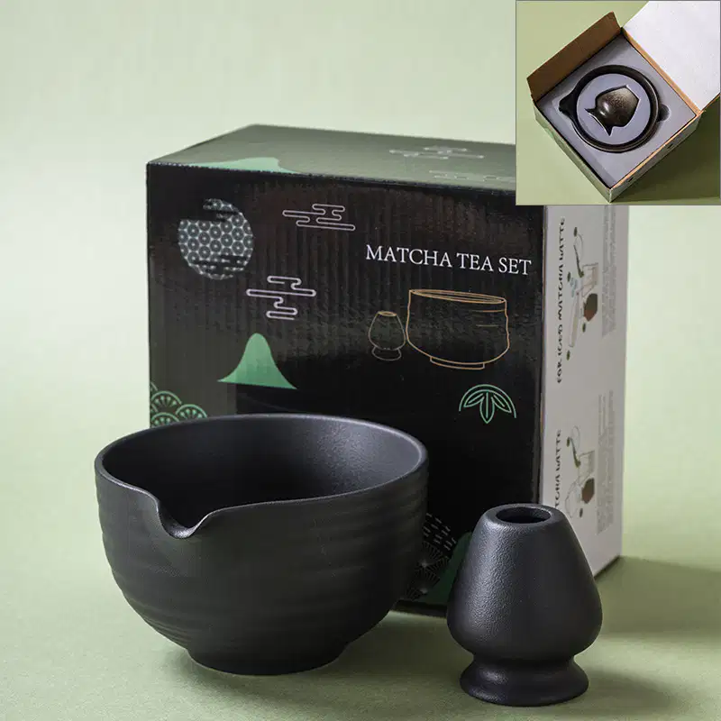 The Matte Matcha Bowl & Whisk Holder Set – 2 Piece | Matte Black is shown in front of its packaging, with an inset highlighting the set neatly arranged inside the box.