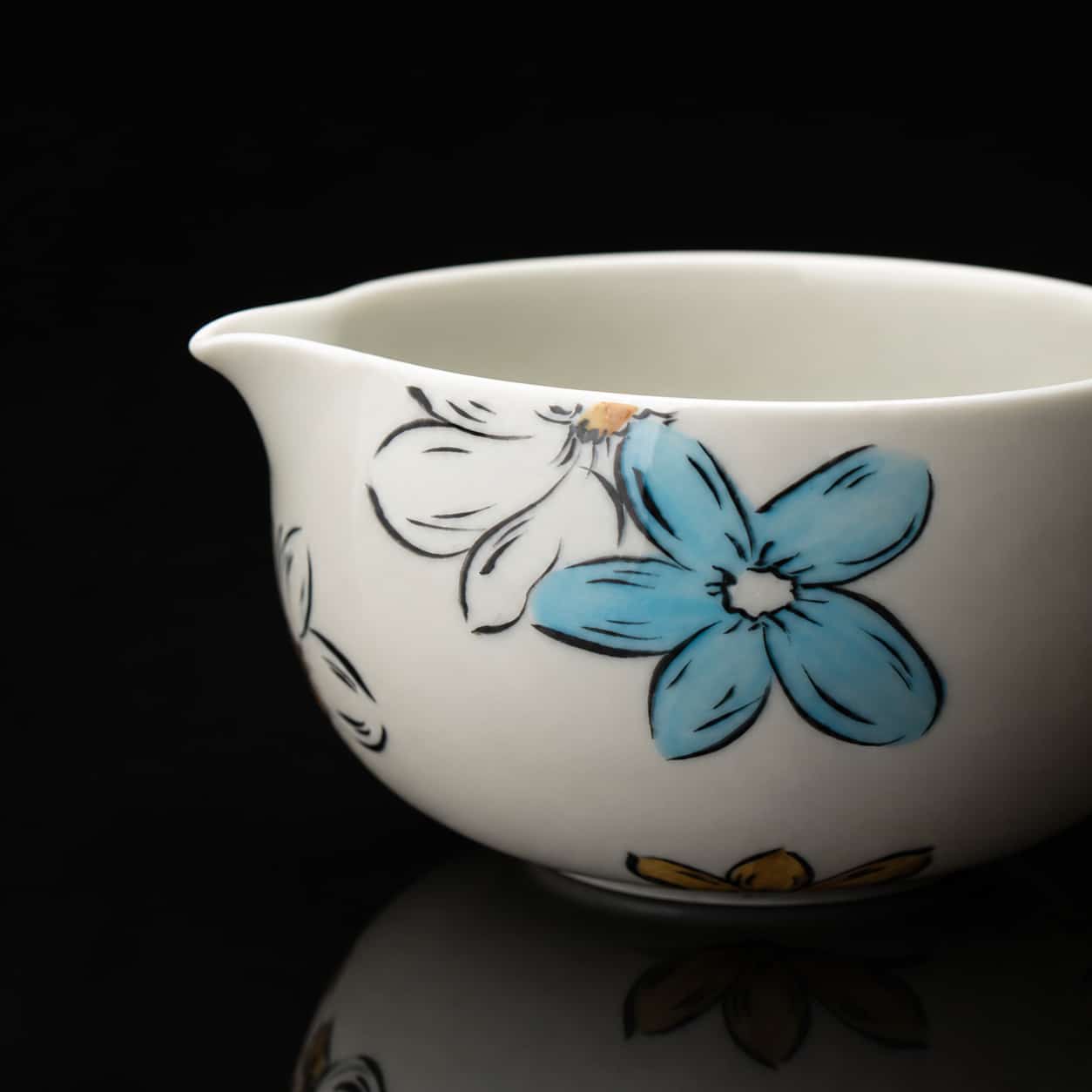 White ceramic jug with hand-painted blue, yellow, and black blossom designs, set against a black background—a perfect complement to any Whisk Gift Set or Matcha Bowl collection.