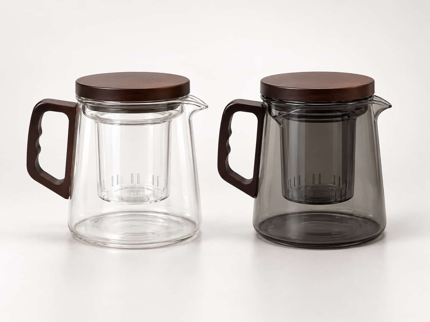 Two borosilicate glass teapots with brown wooden lids and handles, one clear and one tinted grey, each featuring an internal strainer.