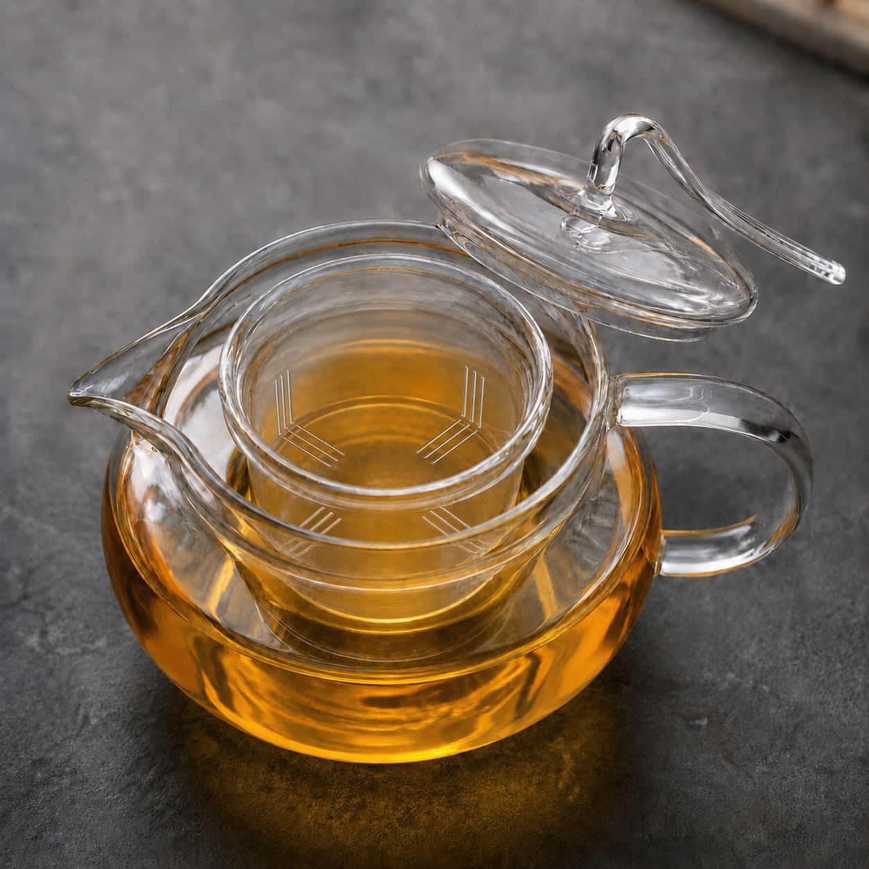The Arc Glass Teapot with Infuser - 600ml, shown here with a lid and filled with amber-coloured tea, sits on a dark surface. Featuring a built-in infuser and curved handle, this elegant teapot is perfect for savouring your favourite blends.