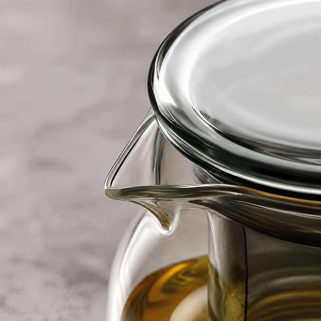 A close-up of the Moya Glass Infuser Teapot with Wooden Lid Detail – 960ml, filled with golden liquid and placed on a light-coloured surface.