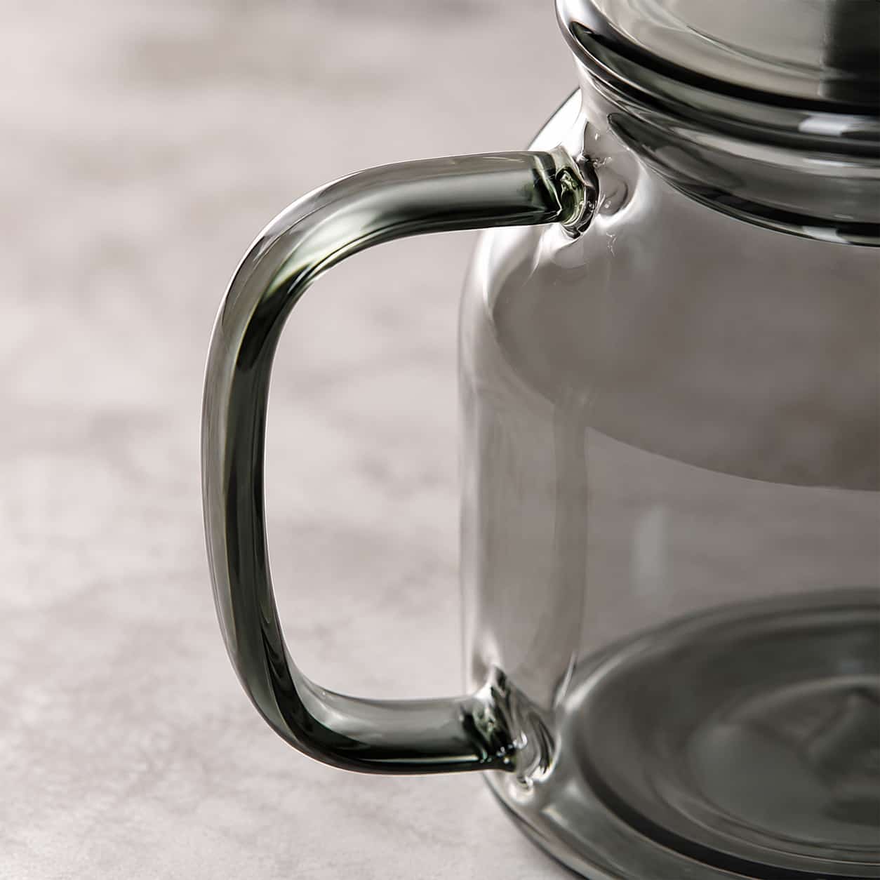 Close-up of the Moya Glass Infuser Teapot with Wooden Lid Detail – 960ml, highlighting the handle and side of the vessel against a softly blurred, light background.
