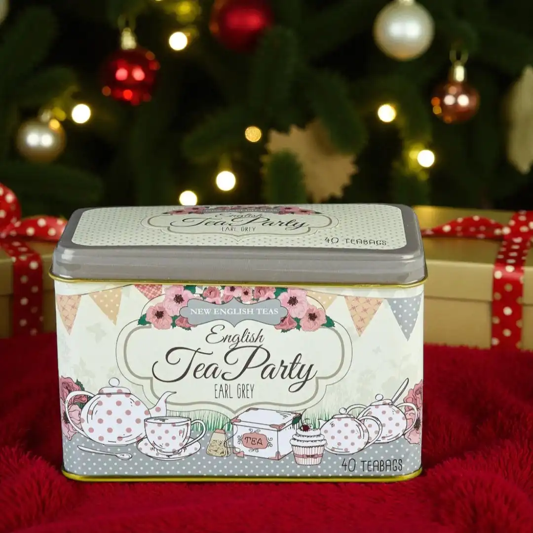 A tin of English Tea Party Earl Grey tea bags sits on a gift box in front of a decorated Christmas tree.