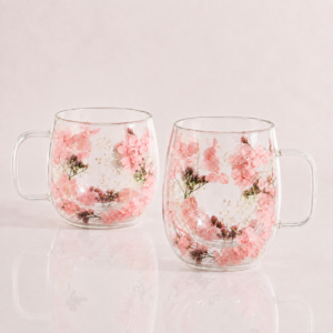 A set of two 400ml Pressed Flower Double-Walled Tea Glasses, featuring embedded pink flowers and green leaves in the glass, displayed side by side on a light pink surface.